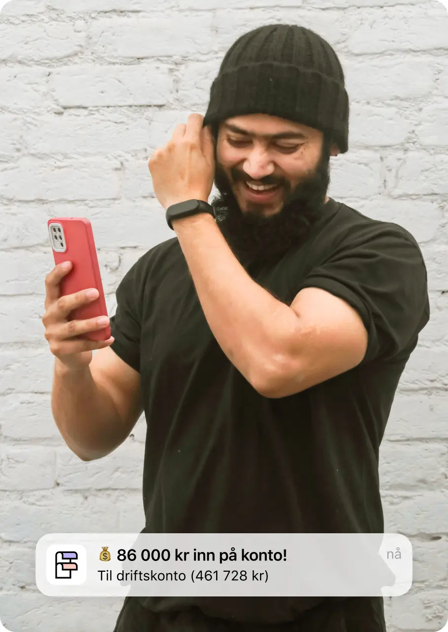 Smilende mann som sjekker mobilen. Varsling som sier «86 000 kr inn på konto!»